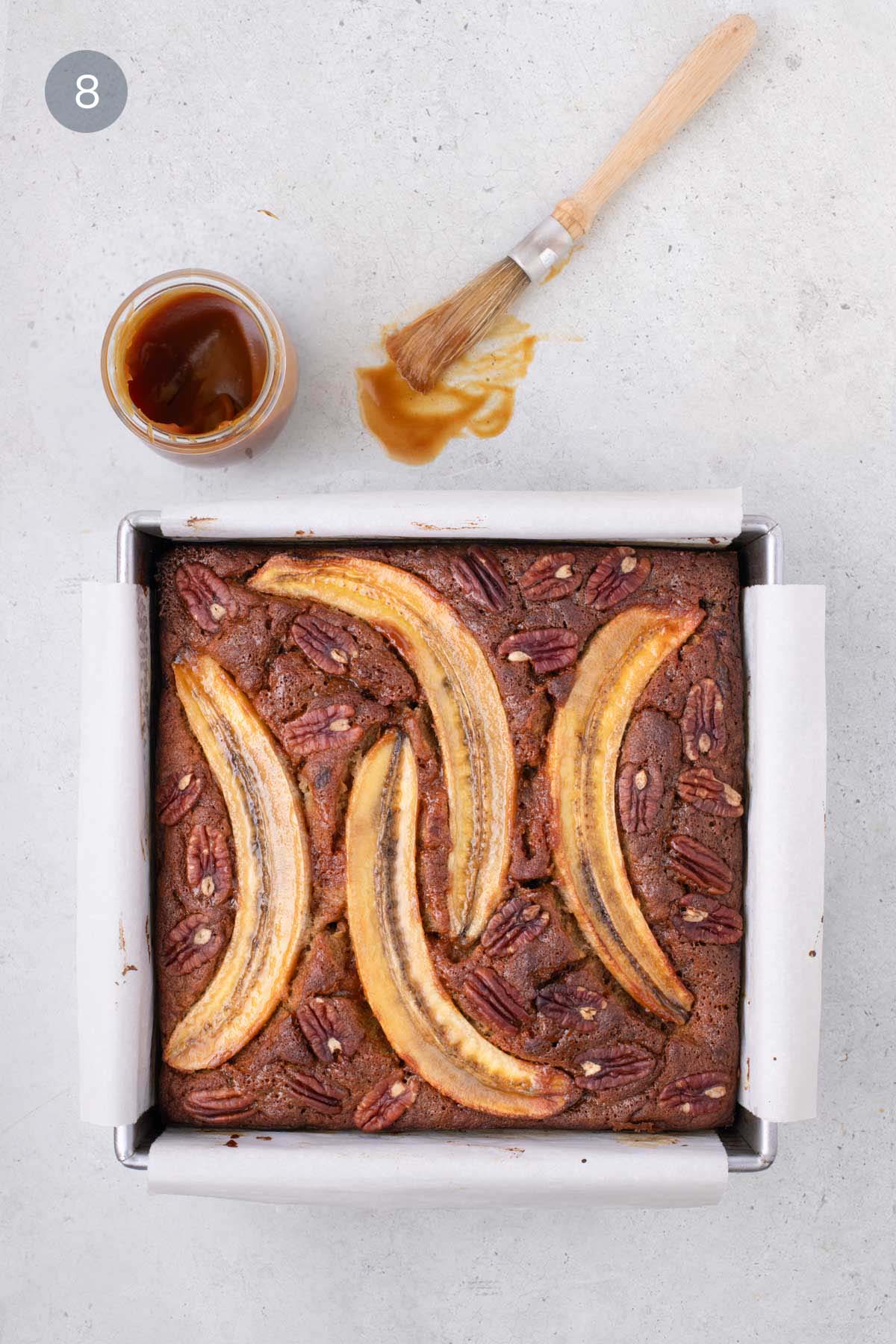 Baked banana bread bars topped with pecans and banana slices, brushed with caramel glaze.