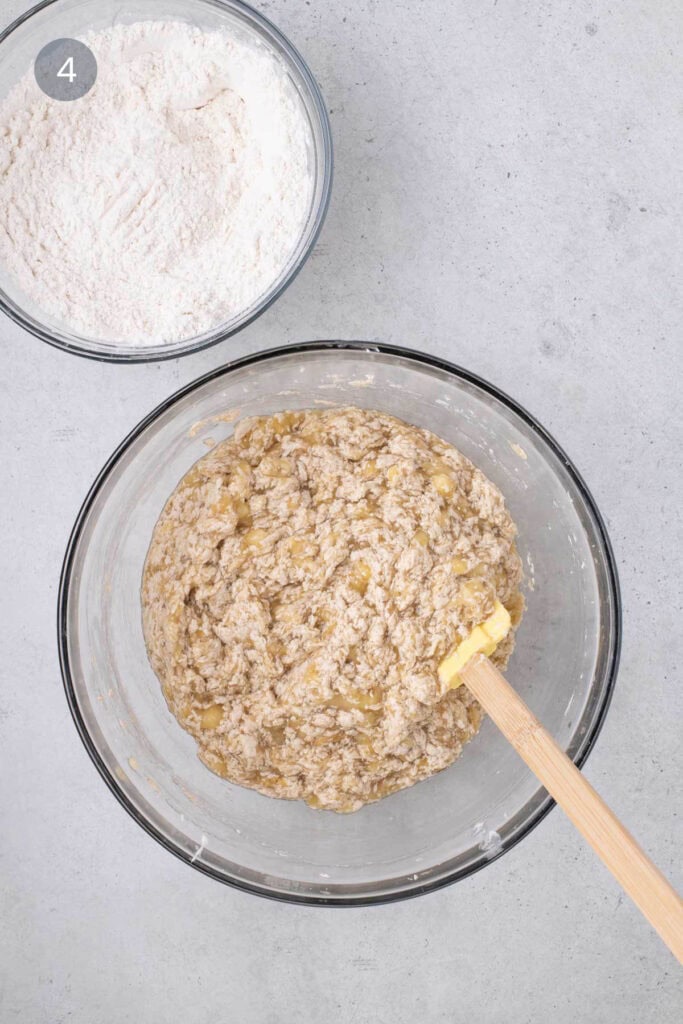 Mashed banana mixture folded into the batter using a wooden spatula.