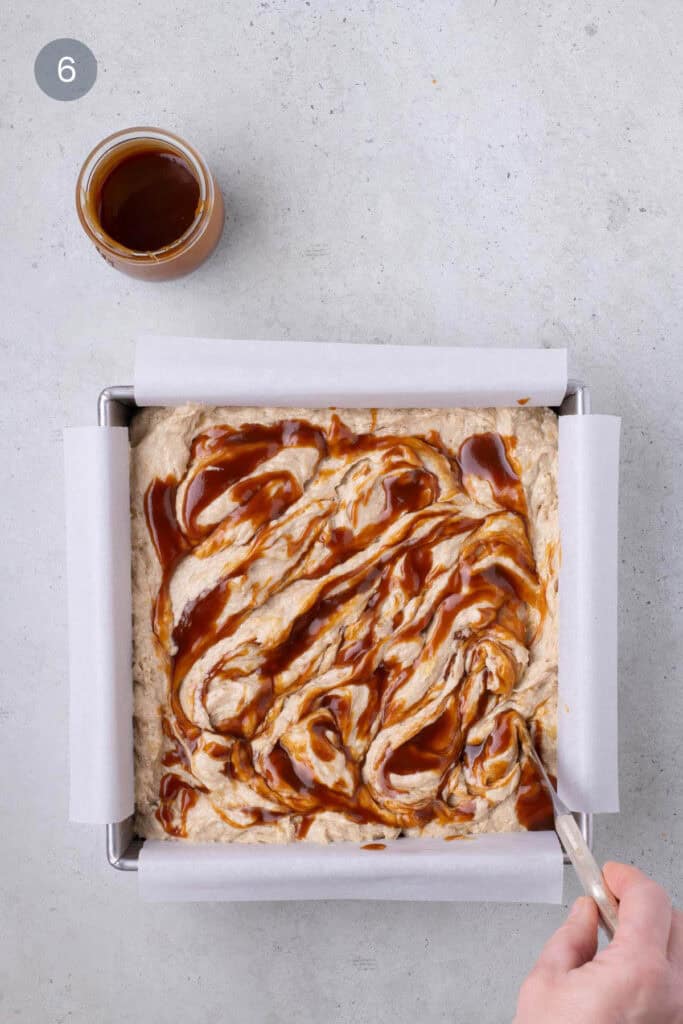 Salted caramel being swirled into banana bread batter with a knife in a square pan.