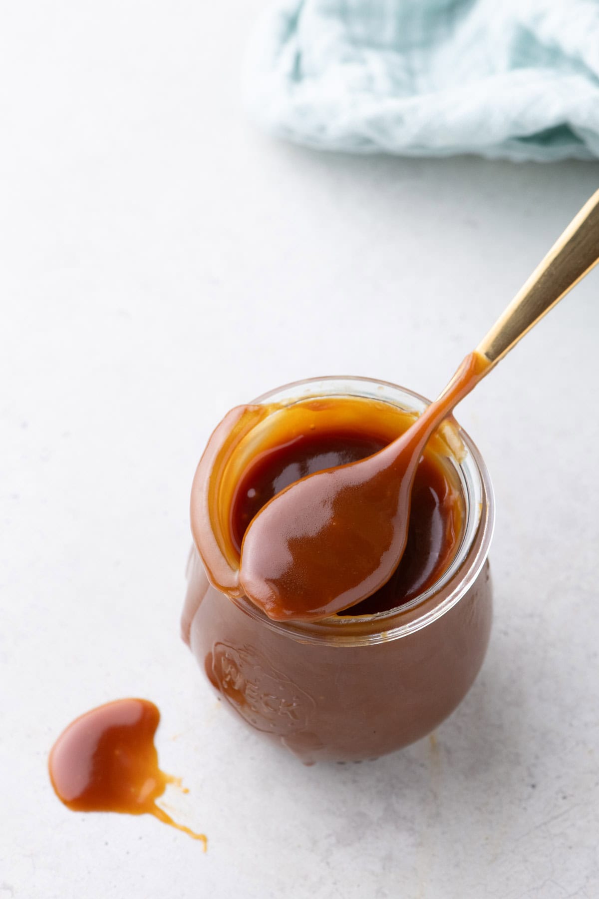 Overhead view of a jar of salted caramel sauce with a spoon and spilled caramel on white surface