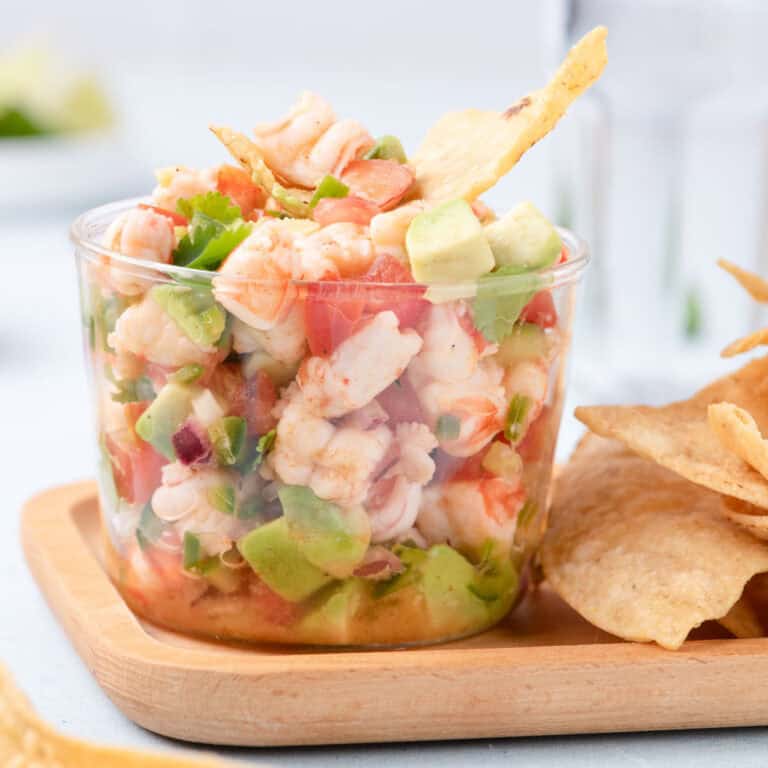 Glass cup filled with fresh shrimp ceviche made with avocado, tomato, red onion, jalapeño, and cilantro, served with tortilla chips.