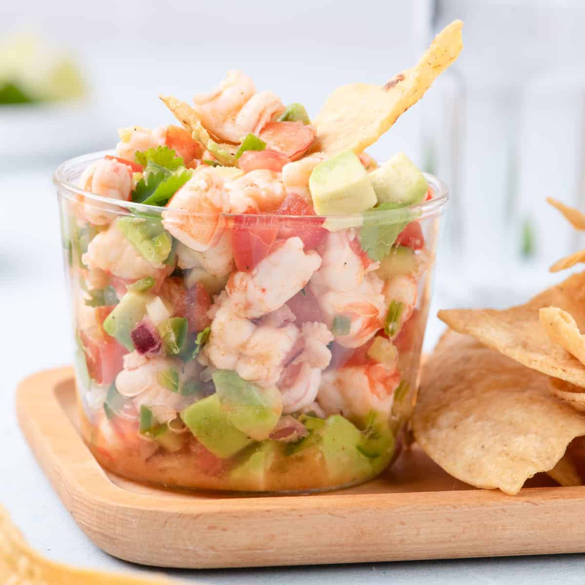 Glass cup filled with fresh shrimp ceviche made with avocado, tomato, red onion, jalapeño, and cilantro, served with tortilla chips.