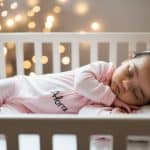 beautiful little baby girl in a crib with text Alora on pajama jumpsuit