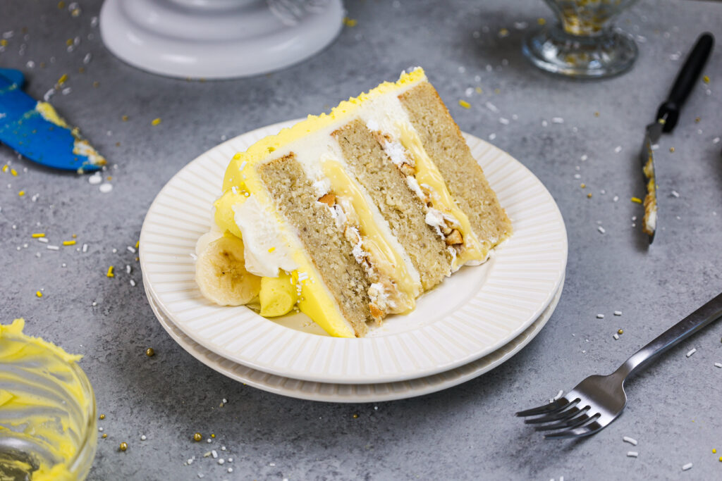 image of a slice of banana pudding cake made with layers of banana cake, pudding, bananas, whipped cream and vanilla wafers