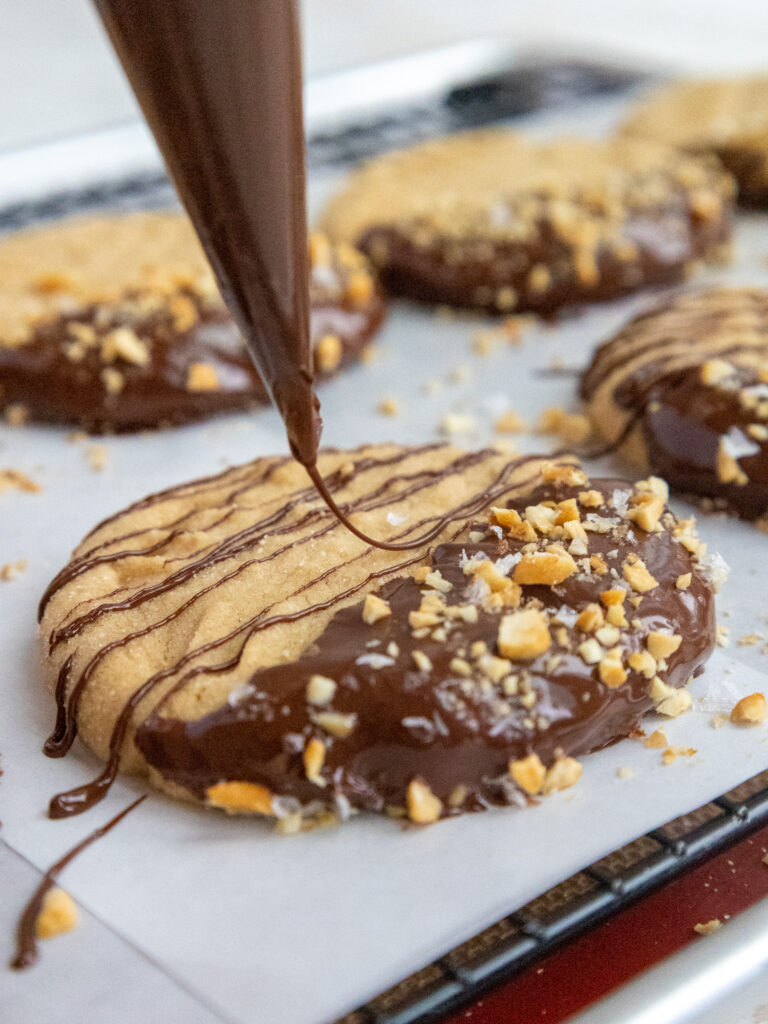 image of melted chocolate being drizzled onto soft batch peanut butter cookies