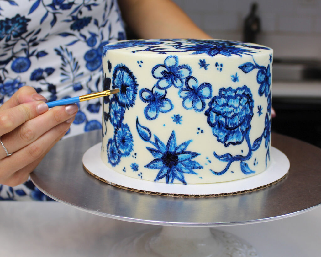 image of a painted buttercream cake decorated with hand painted blue flowers using gel food coloring and vodka to make edible paint