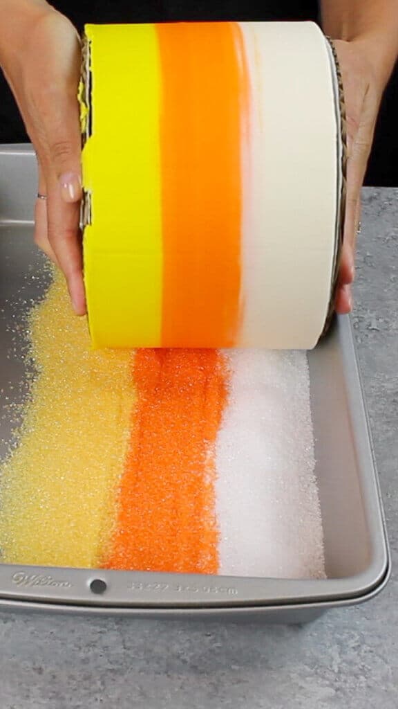 image of cake bring rolled in sanding sugar sprinkles, to decorate the sides of the cake