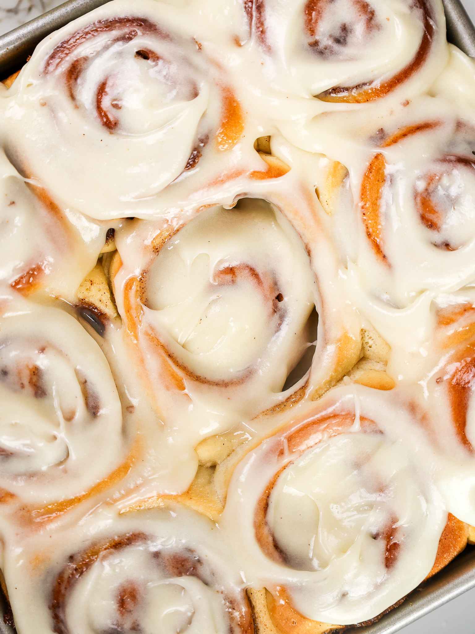 image of cream cheese frosting being added to cinnamon rolls