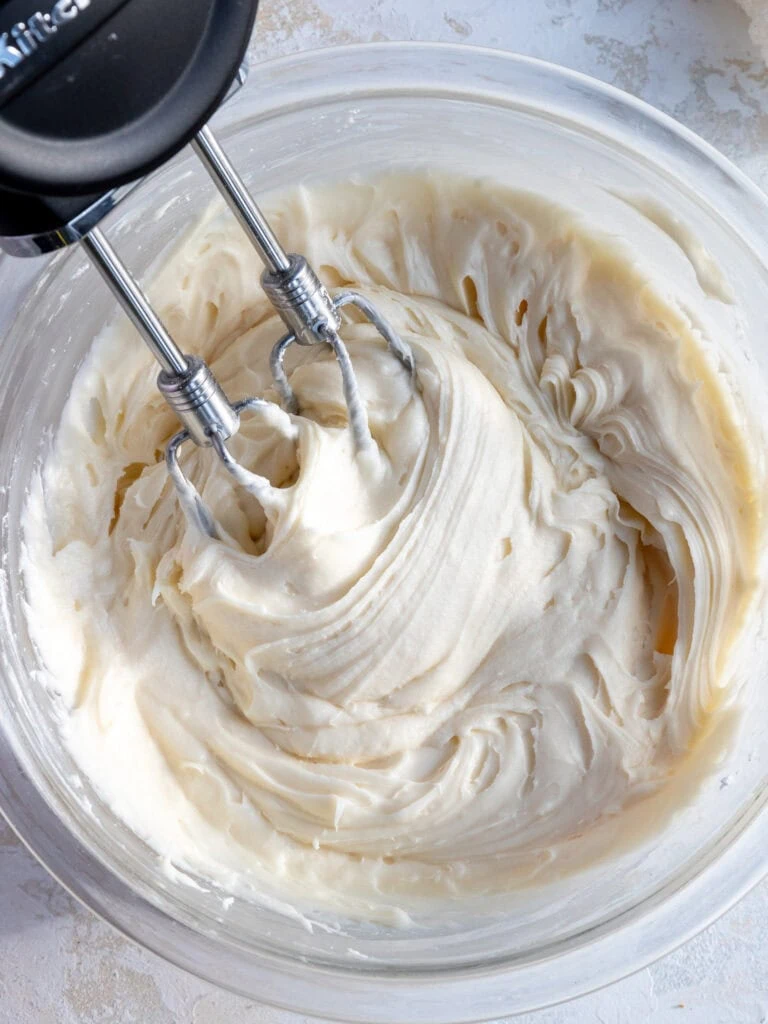 image of cream cheese frosting being mixed in a glass bowl with a hand mixer
