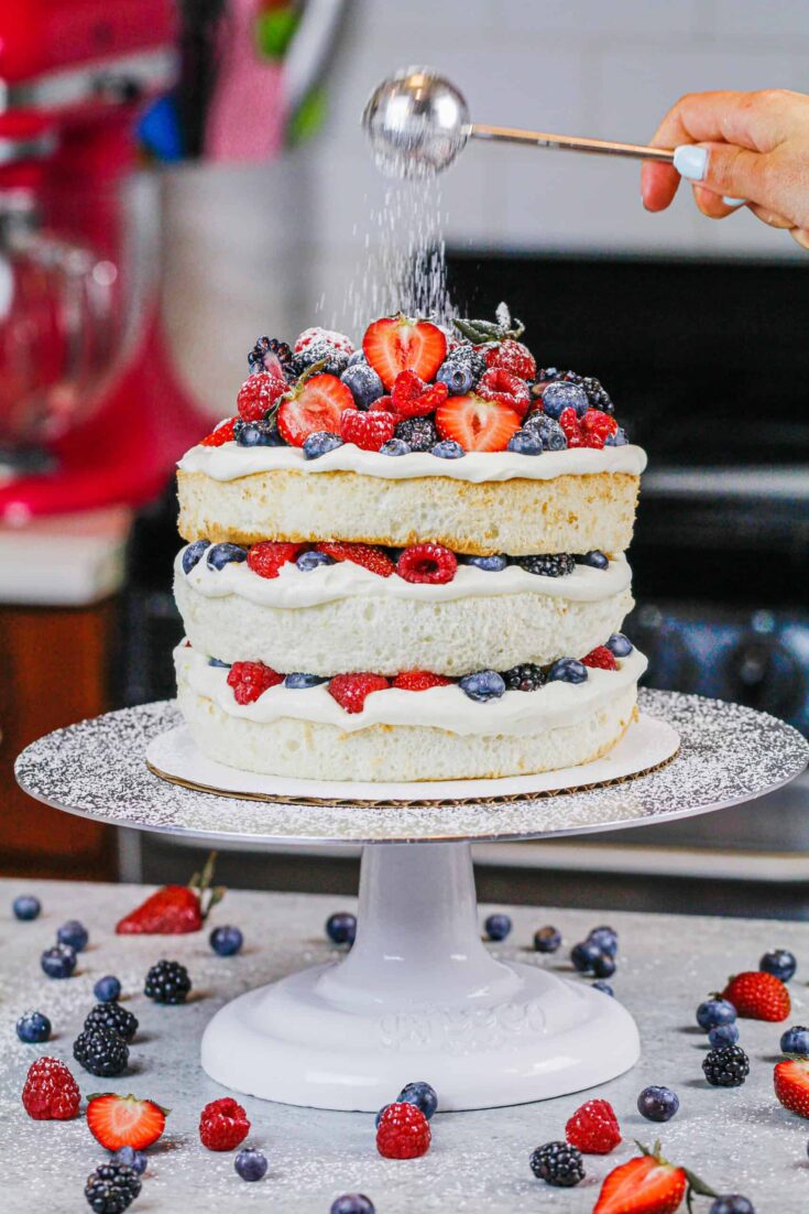 image of a layered angel food cake decorated with fresh berries and dusted with powdered sugar