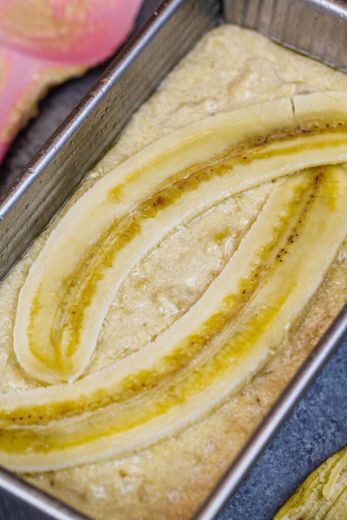 image of banana bread batter in loaf pan topped with extra sugar and sliced bananas to make it look pretty 