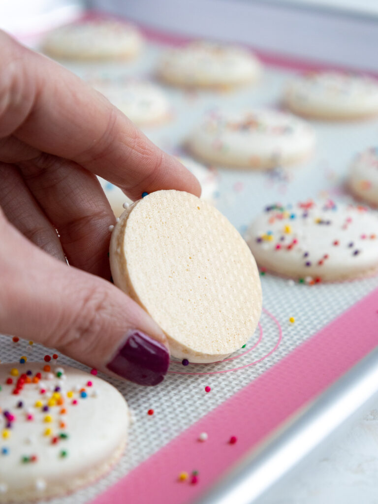 image of a white macaron shell that's being held up to show it's shiny, smooth bottom