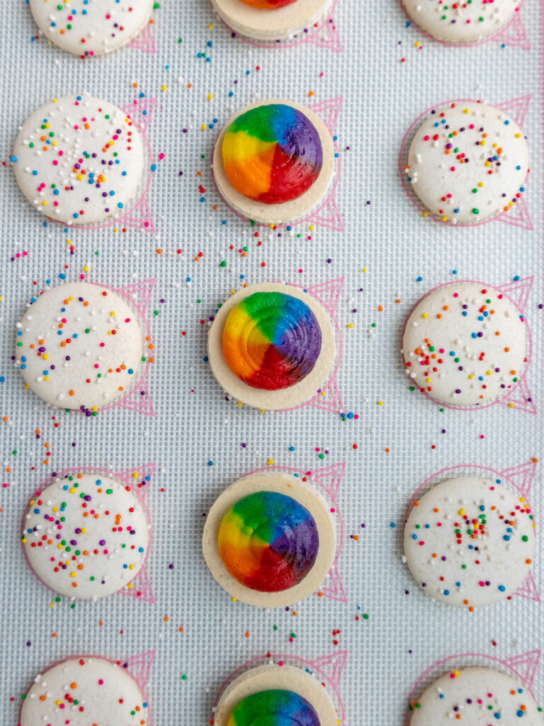 image of rainbow macarons being filled with rainbow buttercream frosting