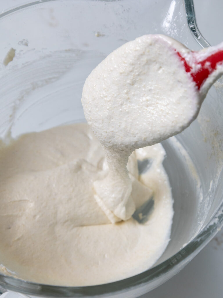 image of white macaron batter being folded until it has the perfect consistency and falls off a spatula in a thick ribbon