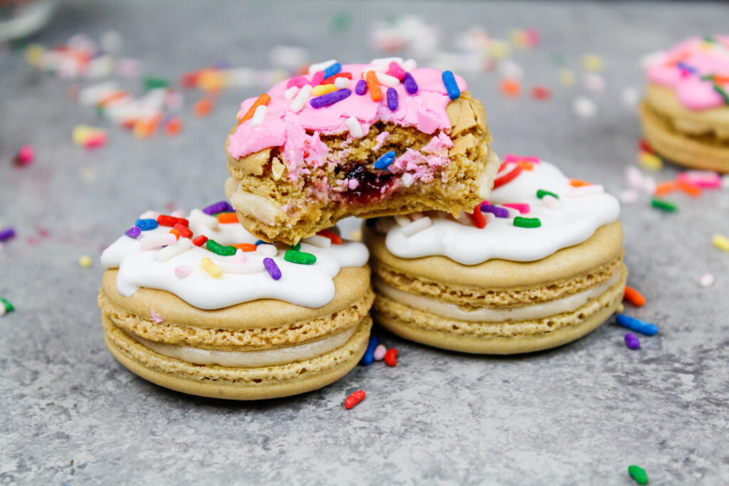 image of a jelly donut macaron that's been bitten into to show it's full shells and delicious filling