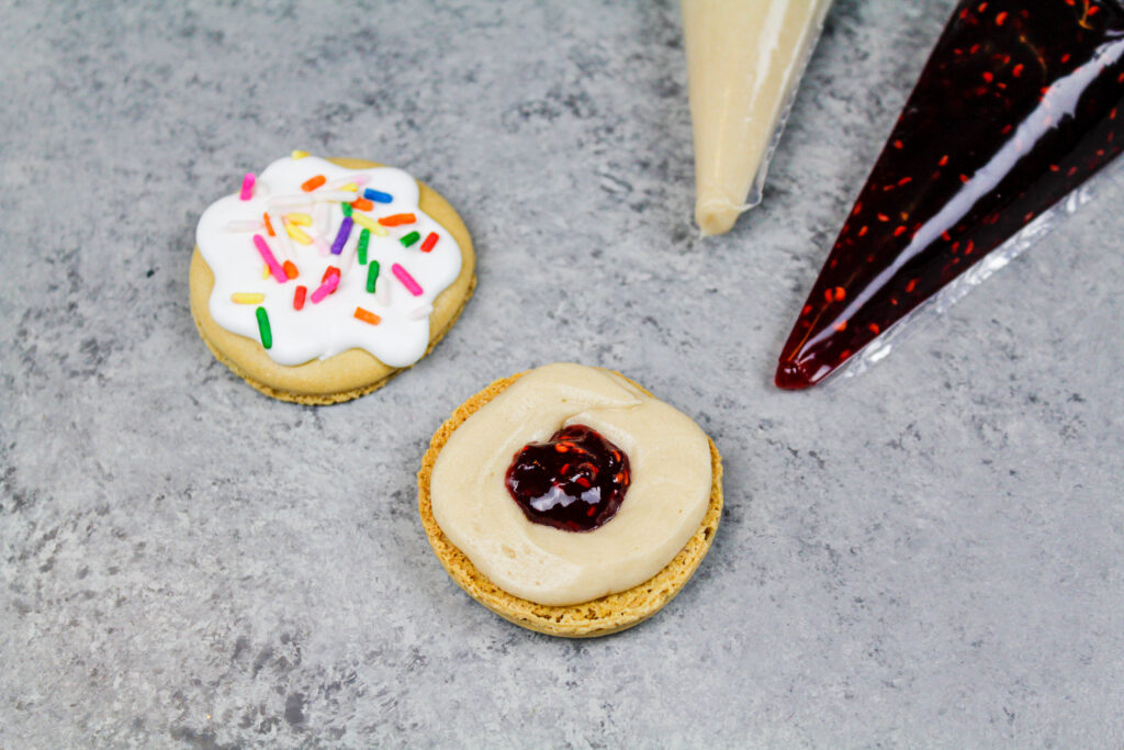 image of a jelly filled donut macaron being made with raspberry jam and maple buttercream