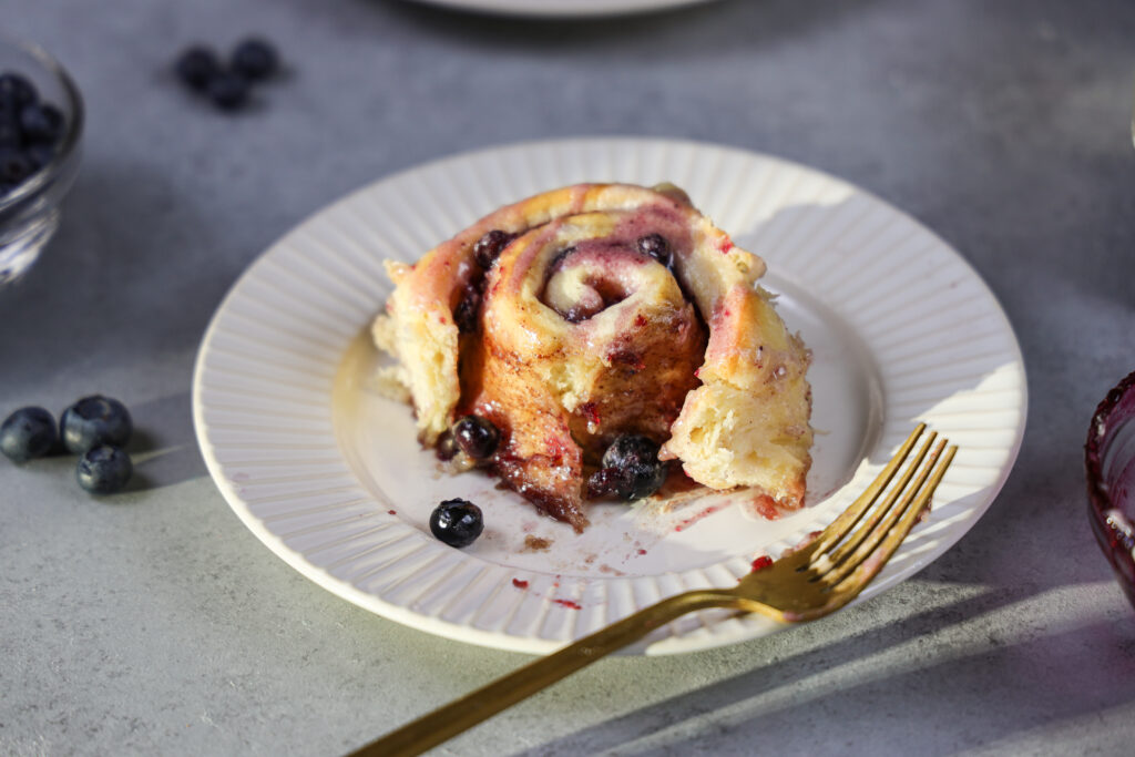 image of a blueberry cinnamon roll on a plate that's been cut into to show how soft and fluffy it is