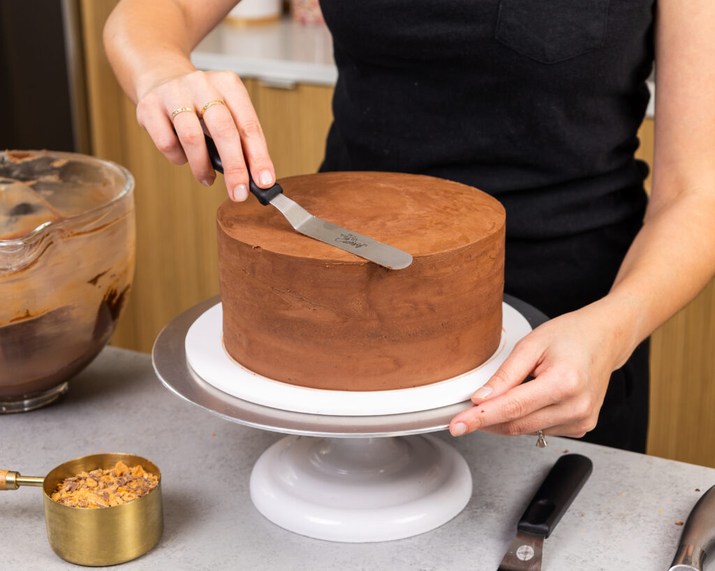 image of a butterfinger cake being frosted with chocolate buttercream frosting