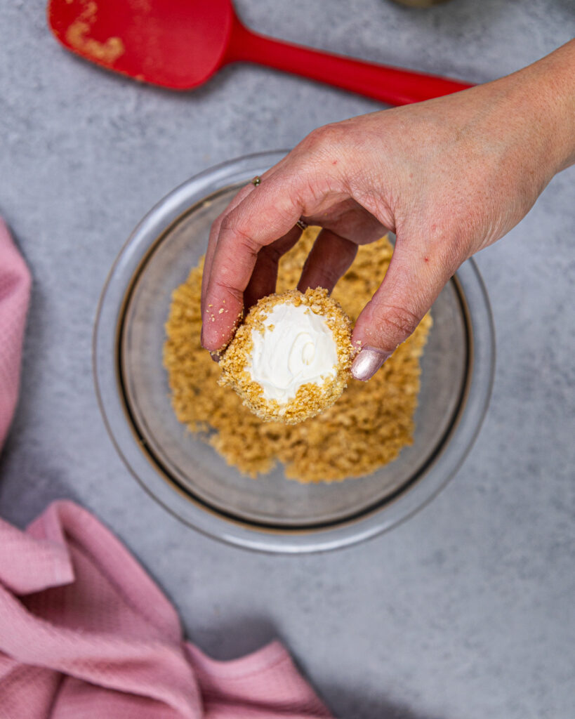 image of a no bake cheesecake bite being held up before being garnished with melted chocolate