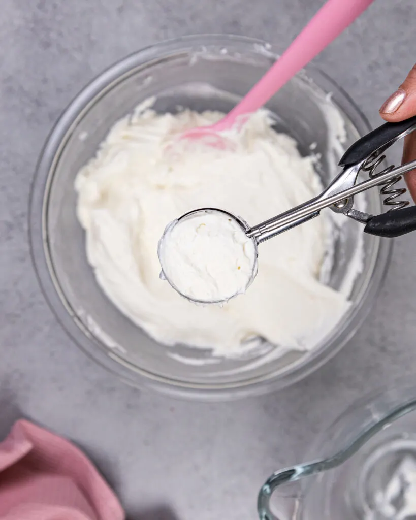 image of a no bake cheesecake filling being scooped using a cookie scoop to make no bake cheesecake bites