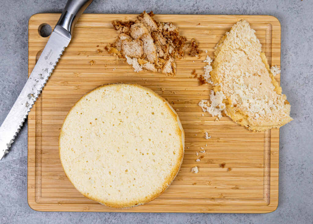 image of a vanilla cake layer being leveled with a serrated knife before being stacked to make a layer cake