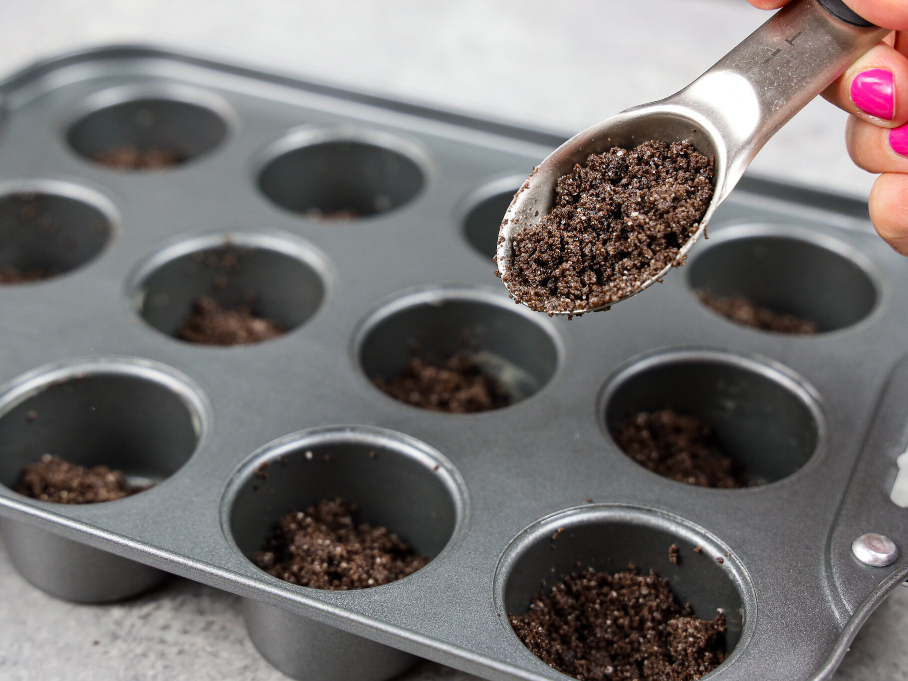 image of oreo cheesecake crust being spooned into a mini cheesecake pan