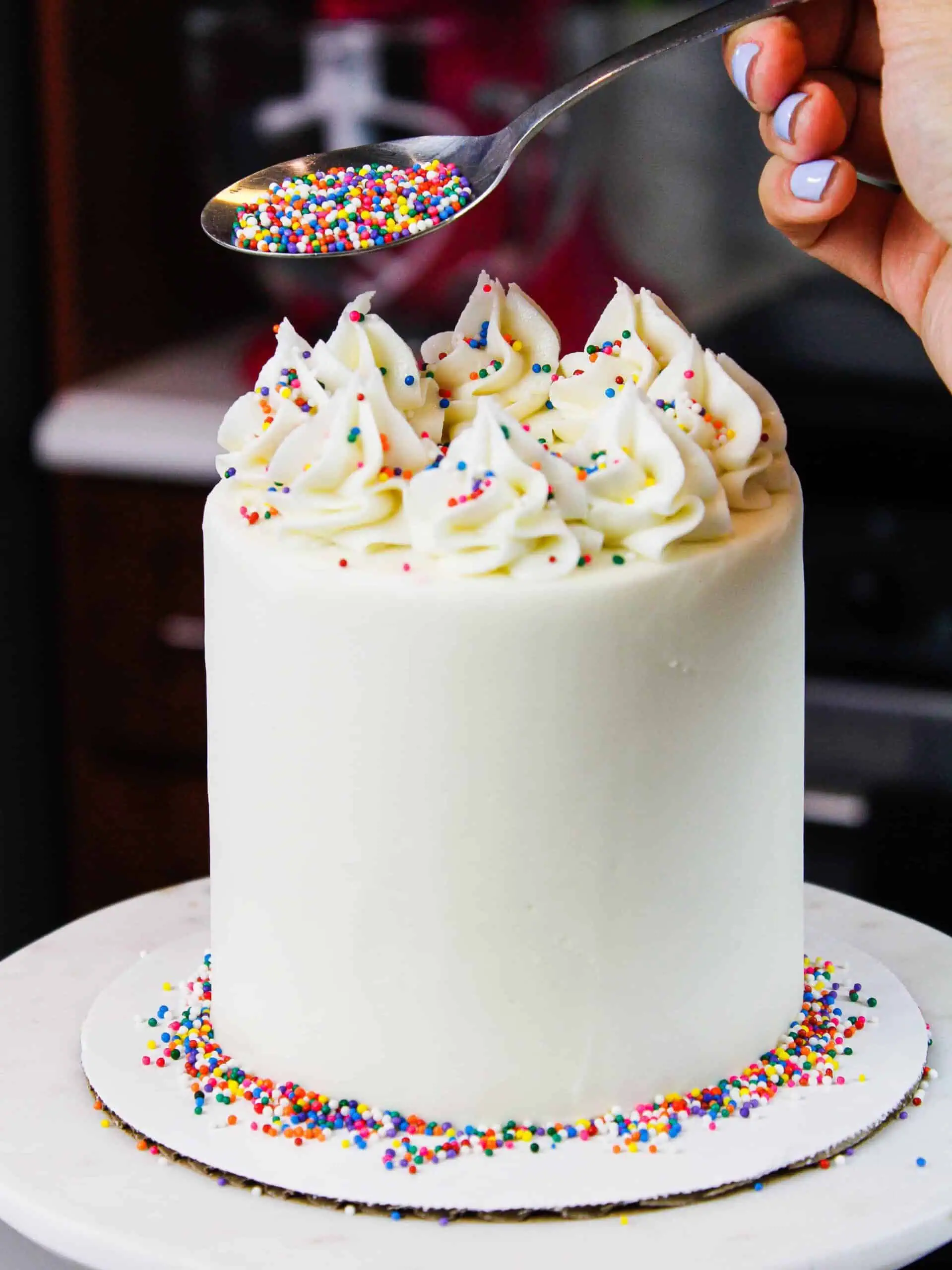 image of mini vanilla cake being decorated with rainbow sprinkles for a birthday