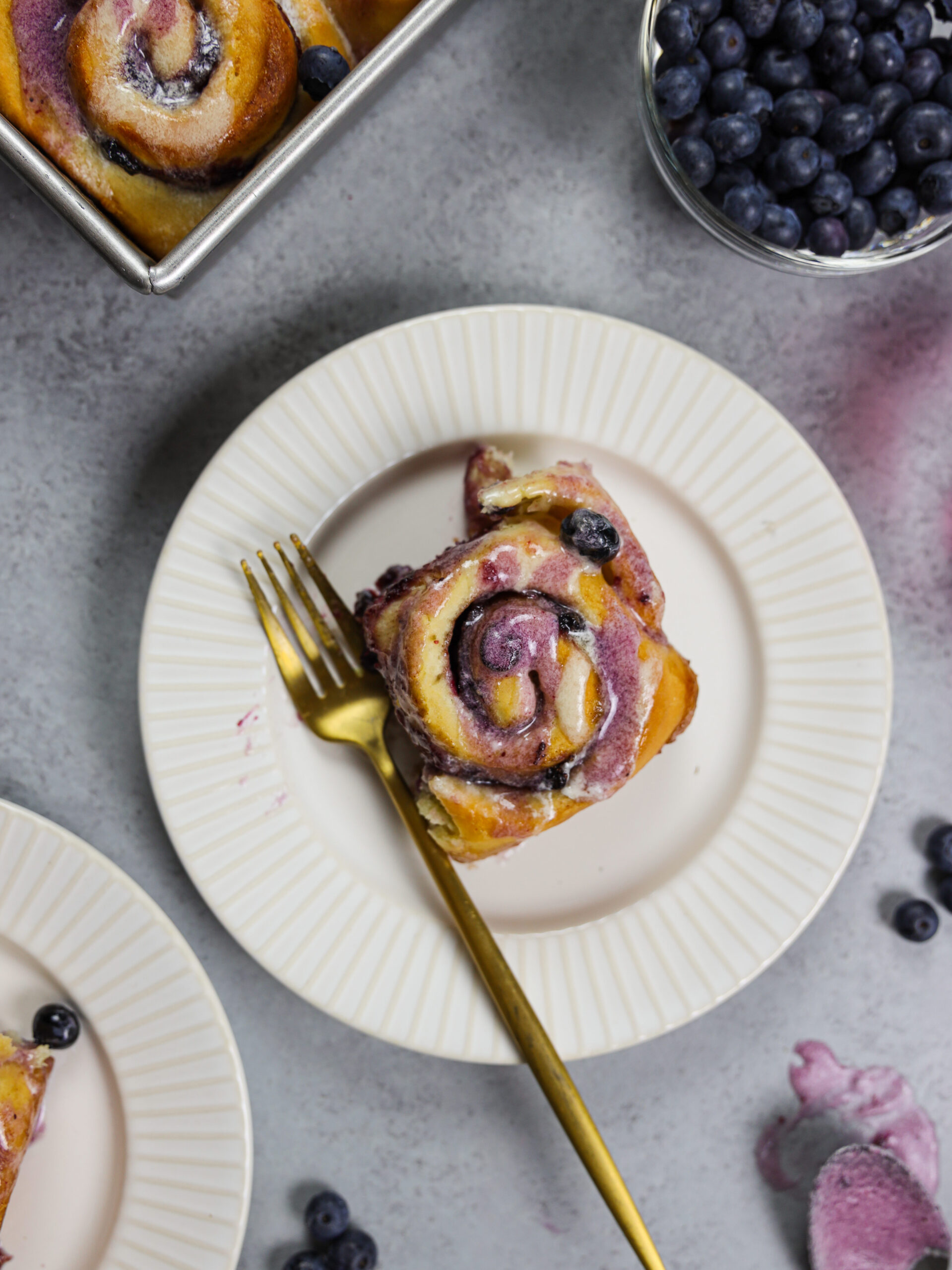 image of a blueberry cinnamon roll on a plate that's been cut into to show how soft and fluffy it is
