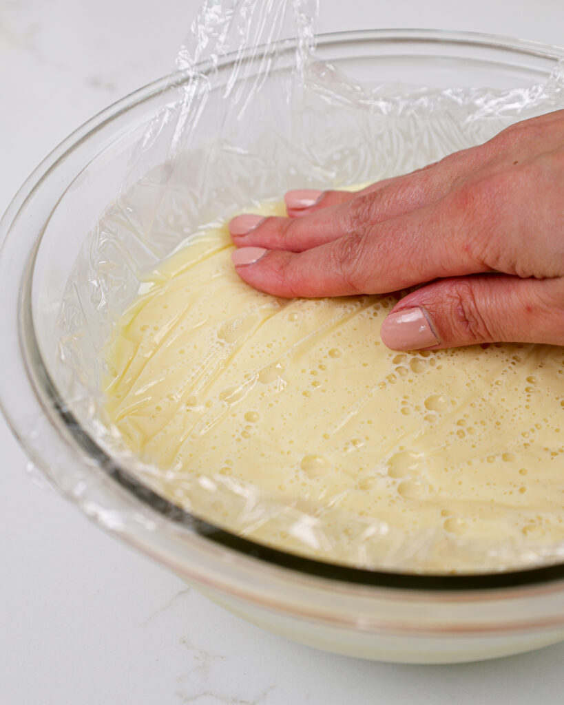 image of white chocolate ganache being covered with plastic wrap before being chilled to prevent it from forming a skin