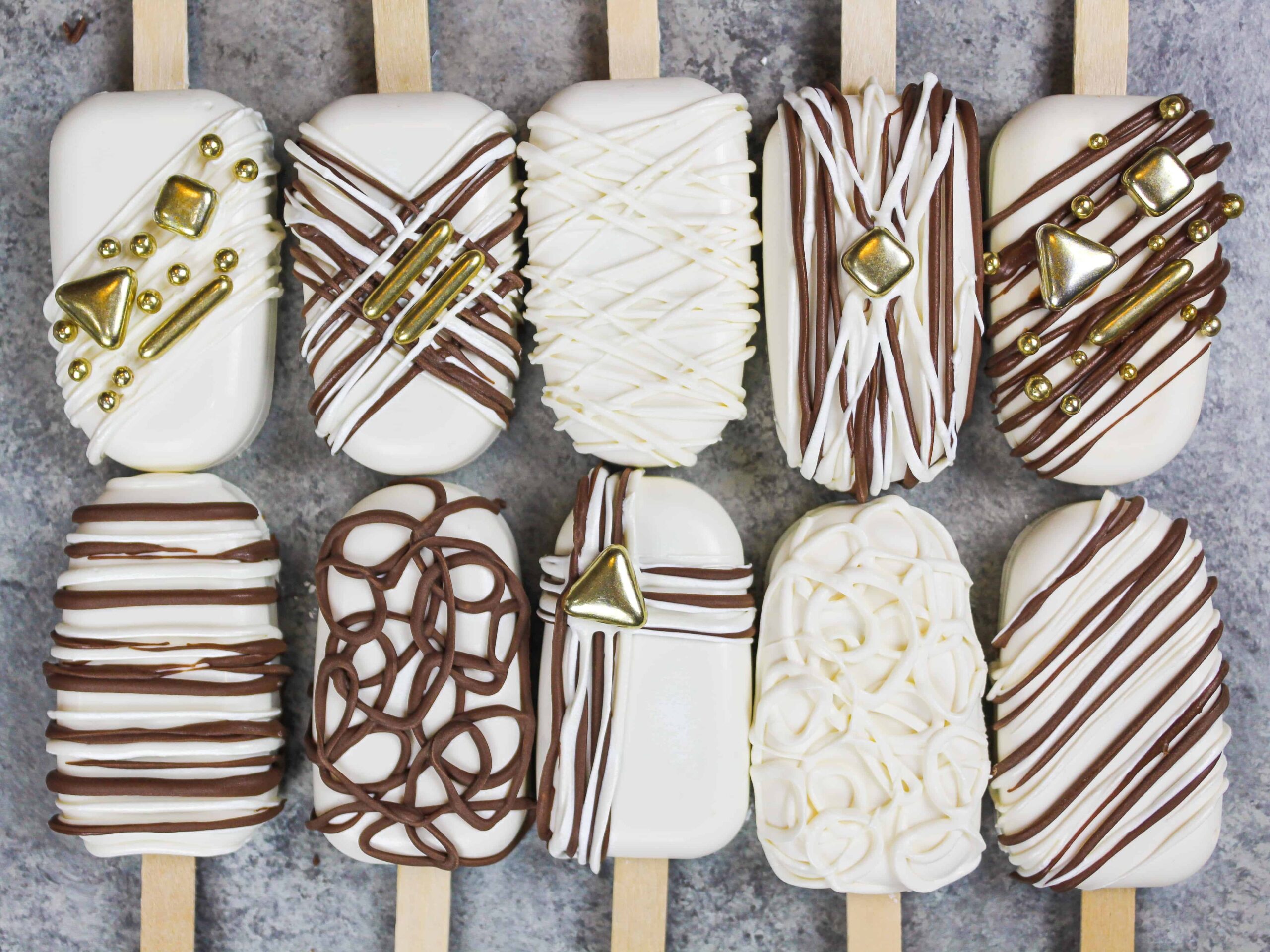 image of cakesicles decorated with white and dark chocolate drizzles and pretty gold sprinkles
