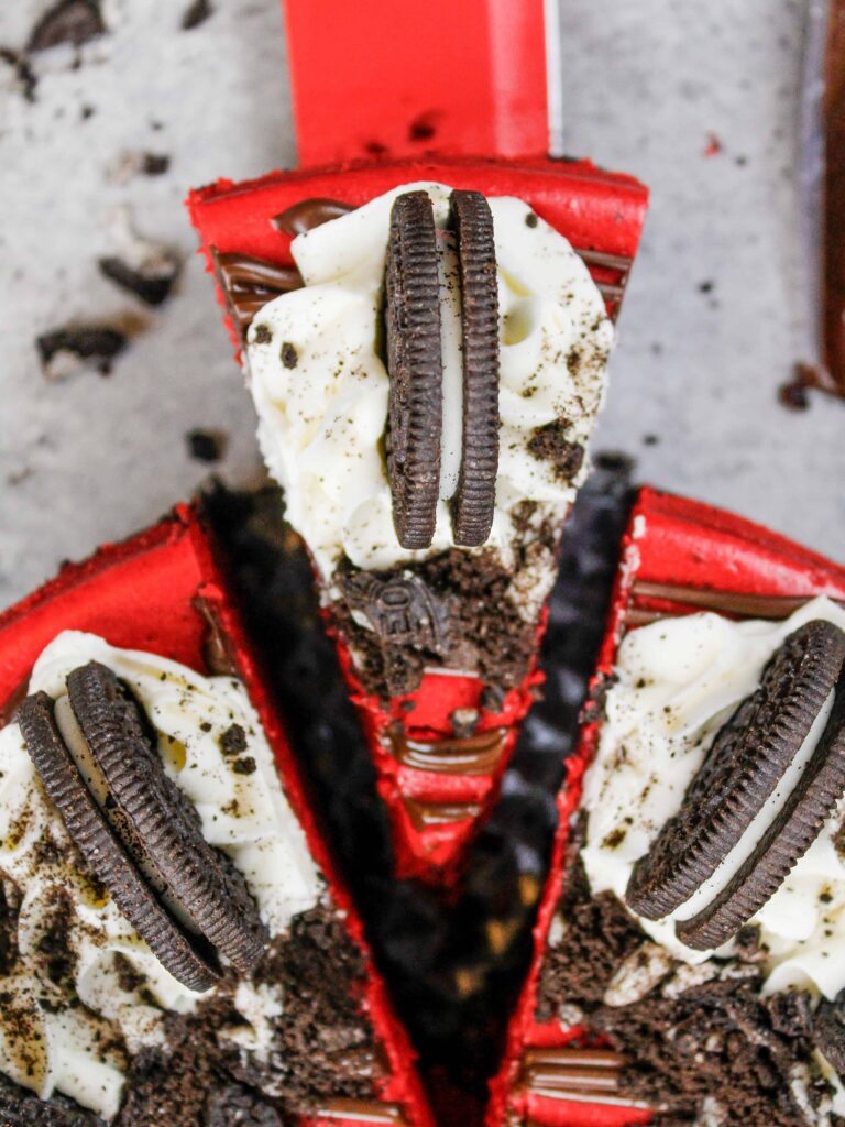 image of red velvet oreo cheesecake that's been cut and is having a slice pulled out to be eaten