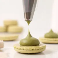 image of matcha ganache being piped on to a matcha macaron shells