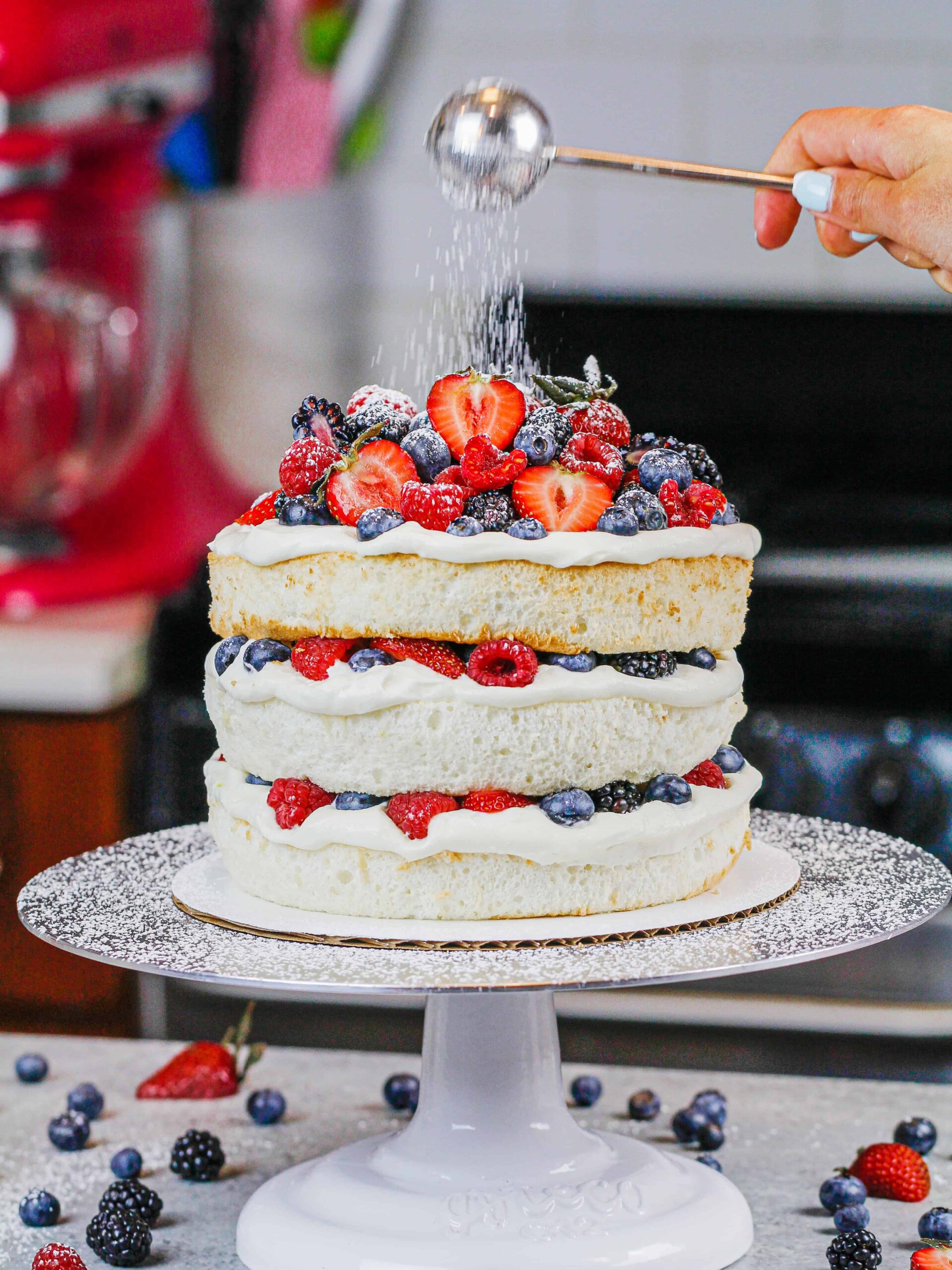 image of a layered angel food cake decorated with fresh berries and dusted with powdered sugar
