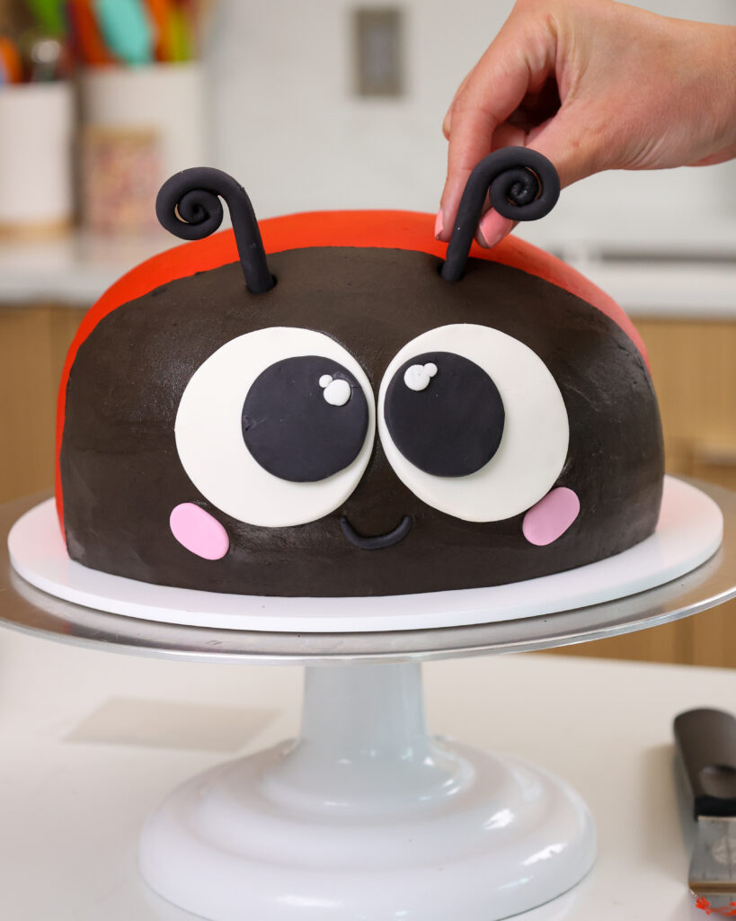 image of fondant antennae being pushed into a lady bug cake