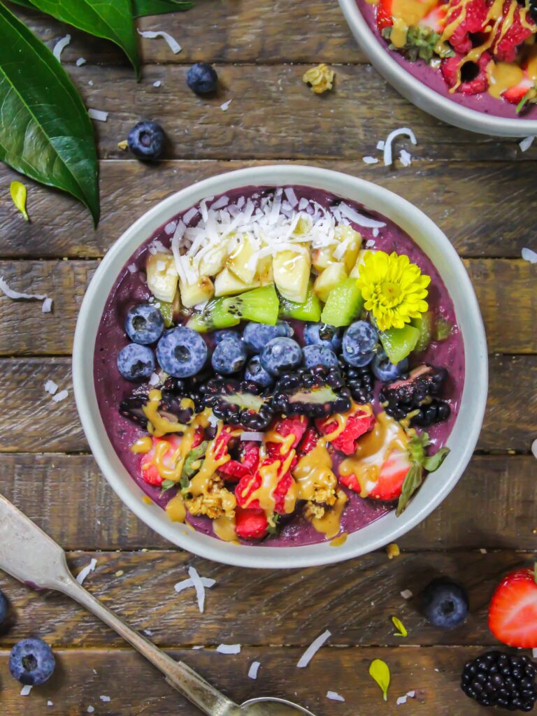 image of pretty peanut butter acai bowl decorate with fresh fruit, granola, and some edible flowers