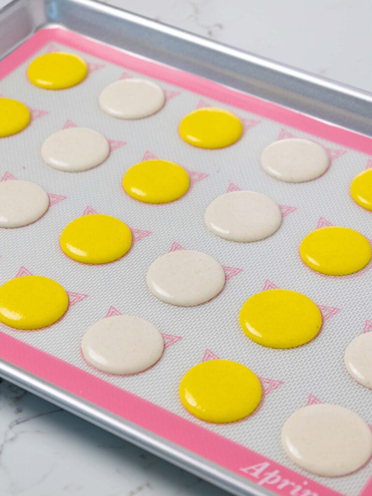 image of yellow and white macaron shells that have been piped on a silpat mat and are resting before being baked