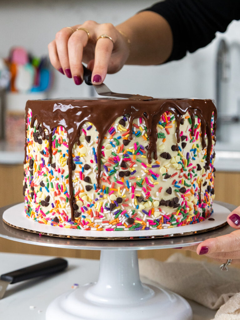 image of chocolate ganache drips being added to a cake with an offset spatula