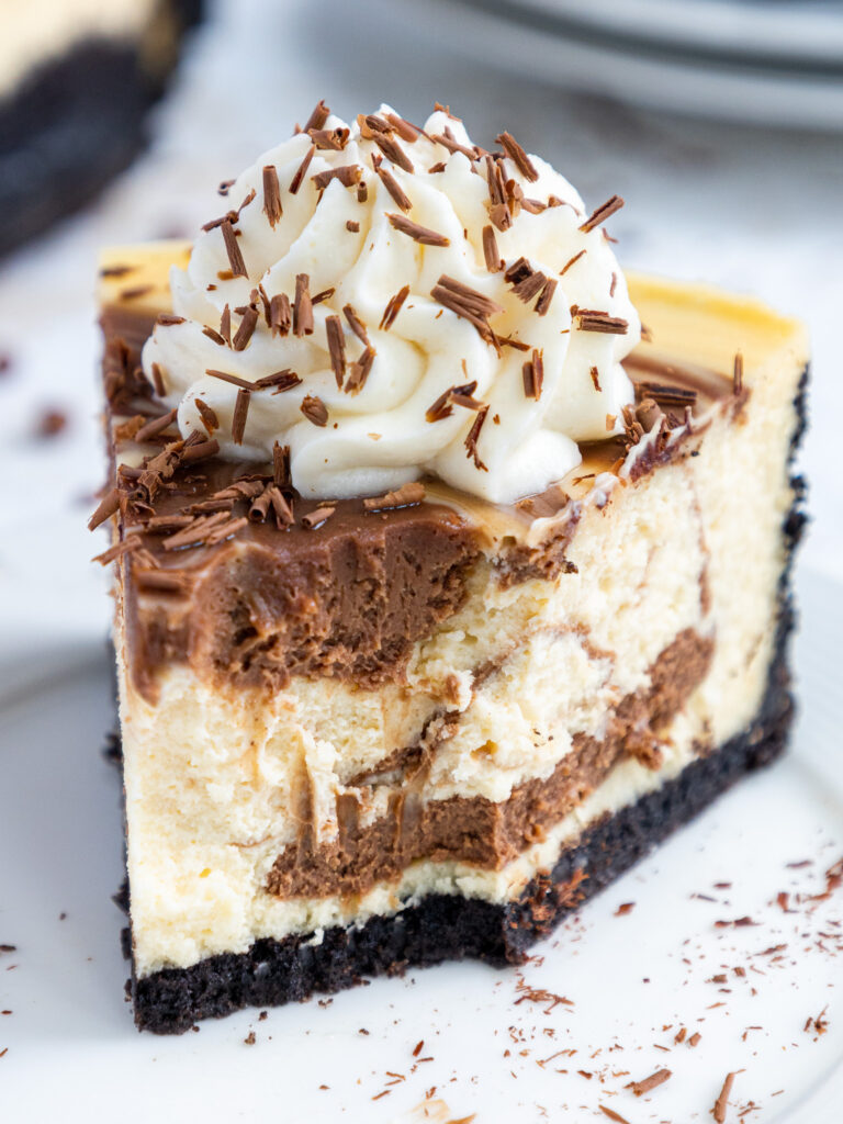 image of a slice of marbled cheesecake on a plate that's been decorated with whipped cream and chocolate shavings