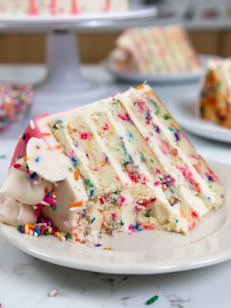 image of a slice of funfetti cake on a plate that's been cut into to show how tender it is