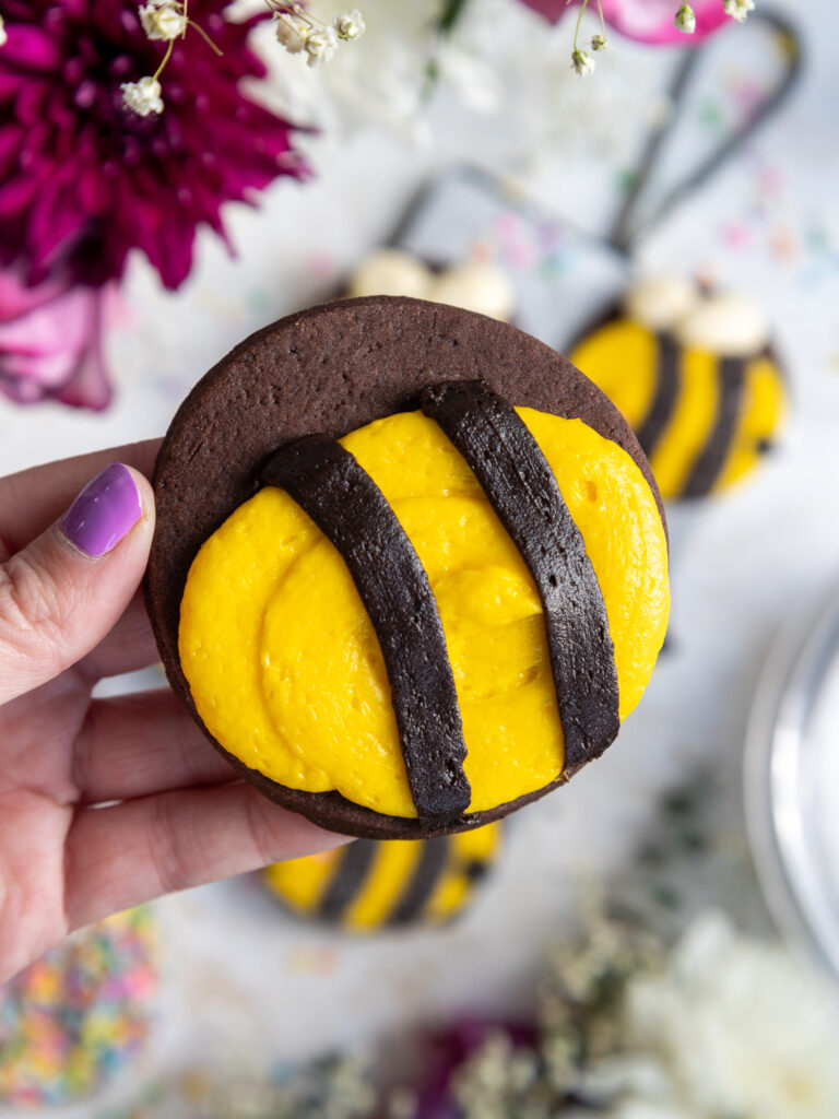 image of frosting being piped onto a dark chocolate cookie to make a cute bumblebee cookie