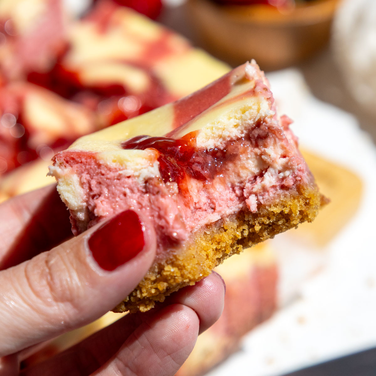 image of a strawberry cheesecake bar that's been bitten into to show it's strawberry and regular cream cheese filling