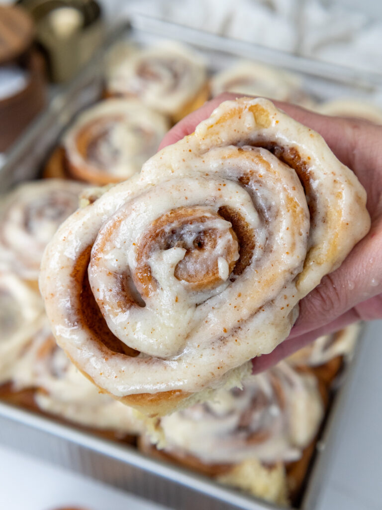 image of a brown butter cinnamon roll being held up and squeezed to show how soft it is