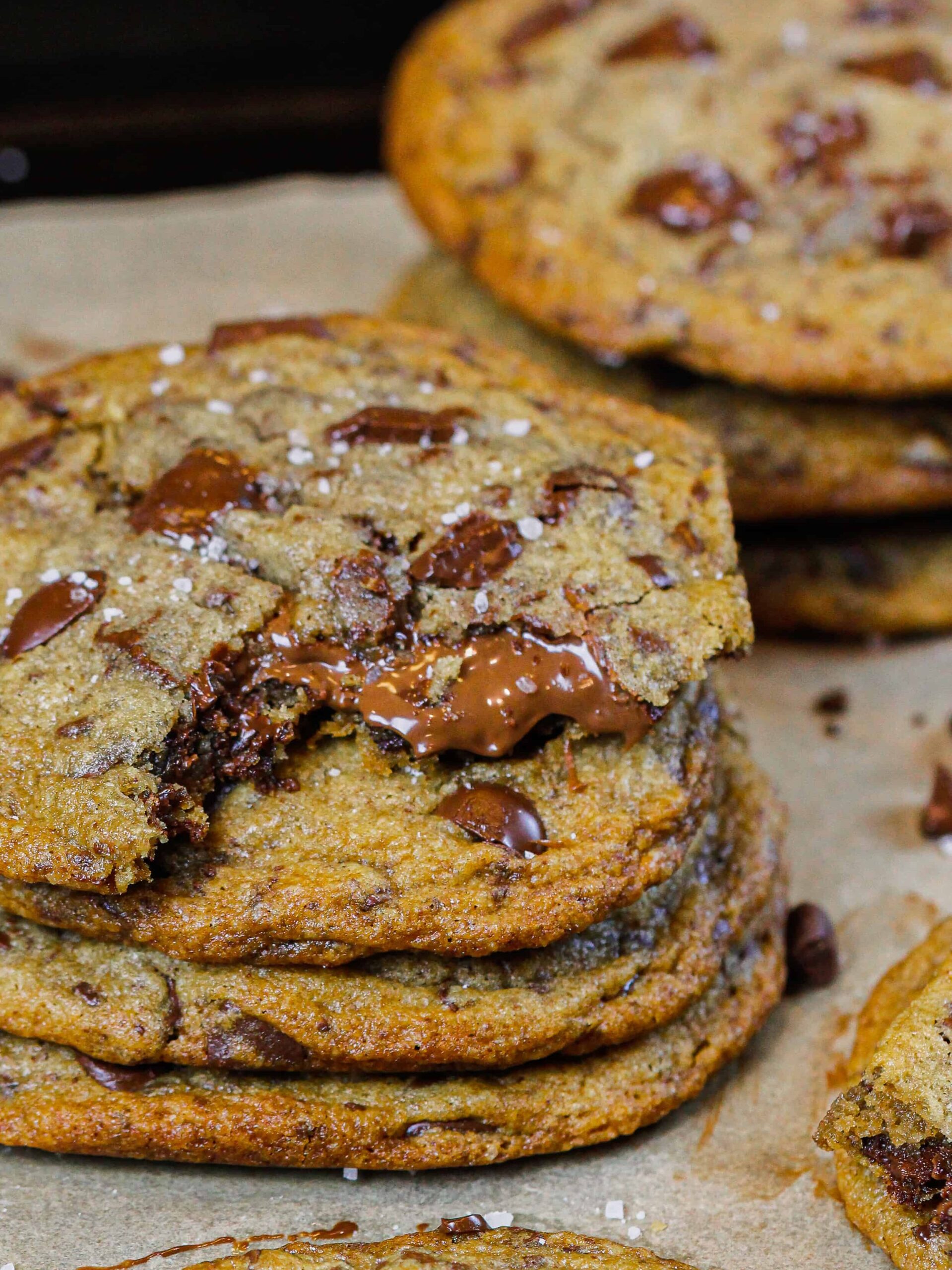 image of stack of brown butter nutella stuffed chocolate chip cookies, with the top cookie bitten into with nutella oozing out
