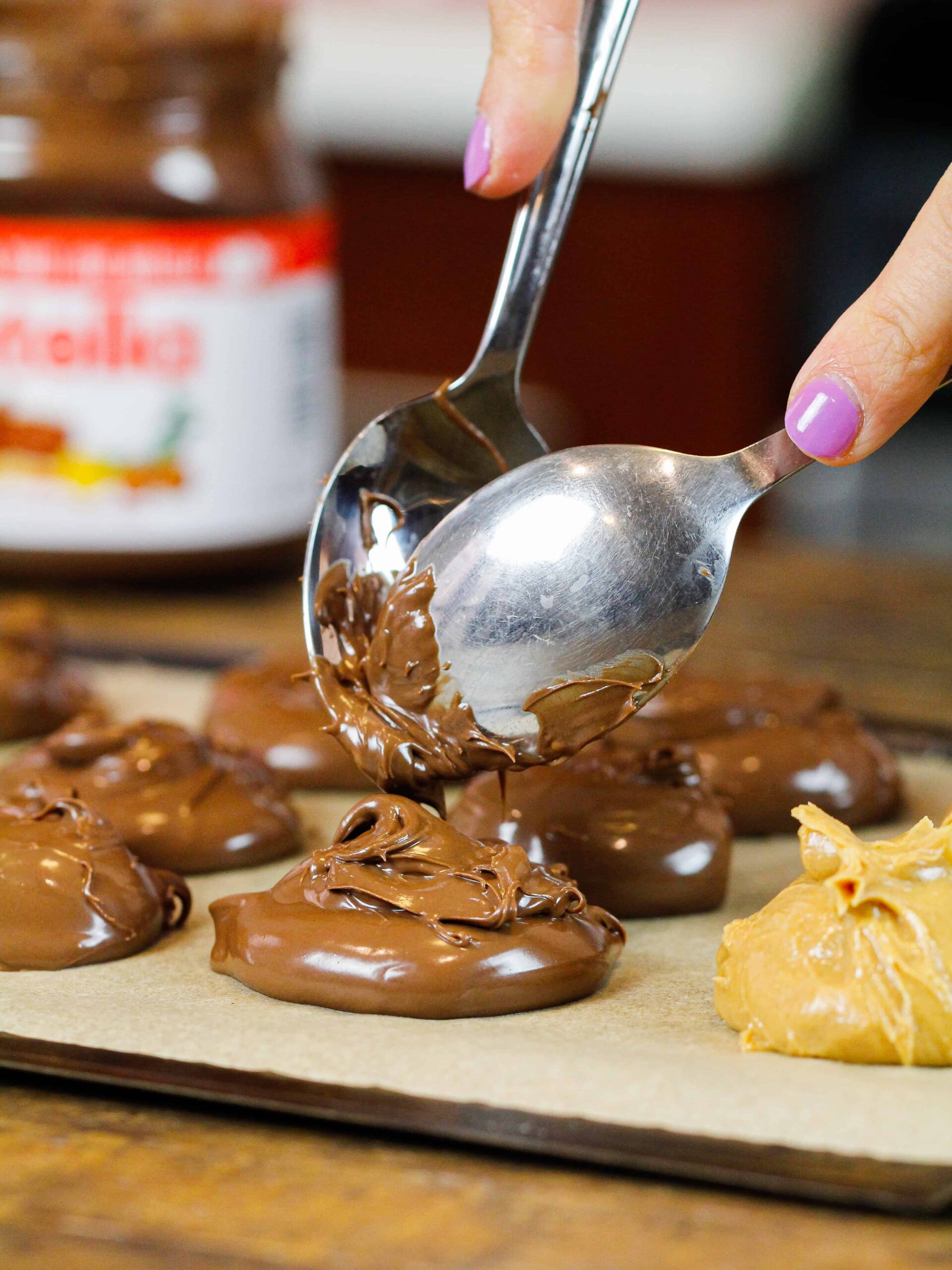 image of nutella being scooped onto a lined pan to chill before being used to fill cookies