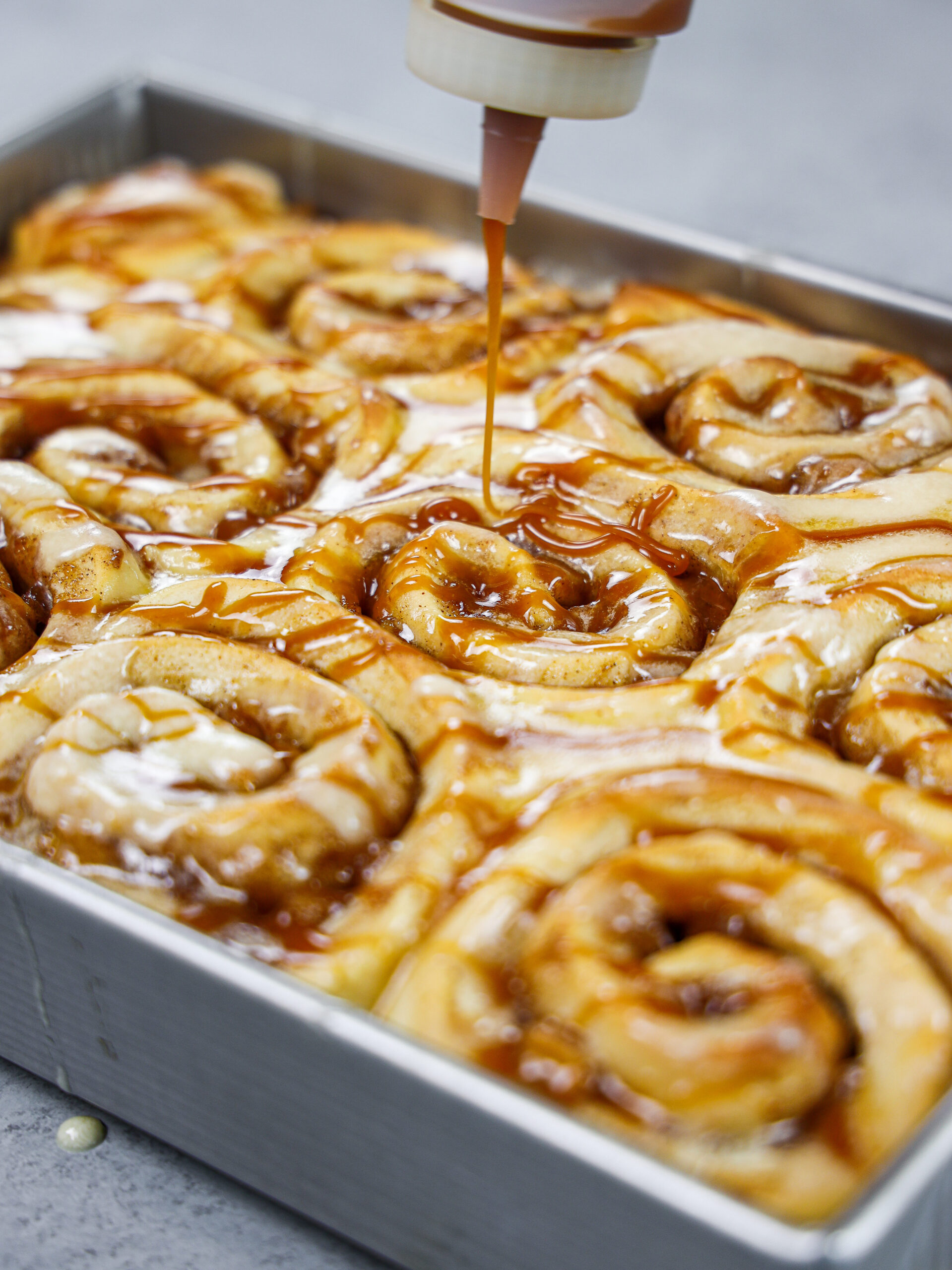 image of caramel being drizzled on top of caramel apple cinnamon rolls