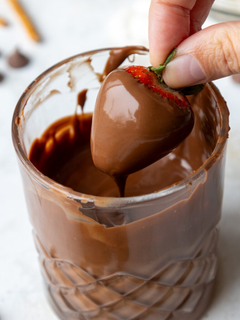 image of a strawberry being dipped in milk chocolate that's been thinned out with a little bit of oil
