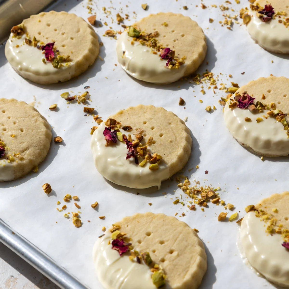 image of white chocolate dipped shortbread cookies that have been decorated with chopped pistachios and dried rose petals