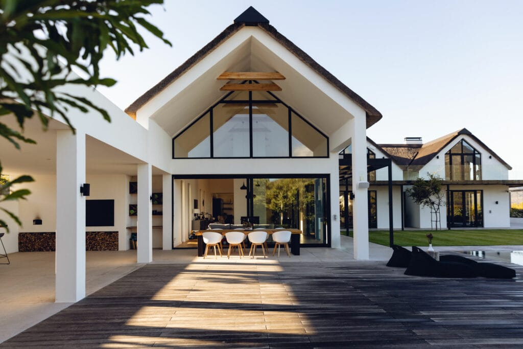 Modern backyard living space, with a wooden patio, two covered living areas, a pool, and windowed walls and pillars