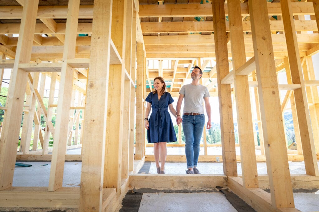 A young couple walking through a newly framed house during a new home construction.
