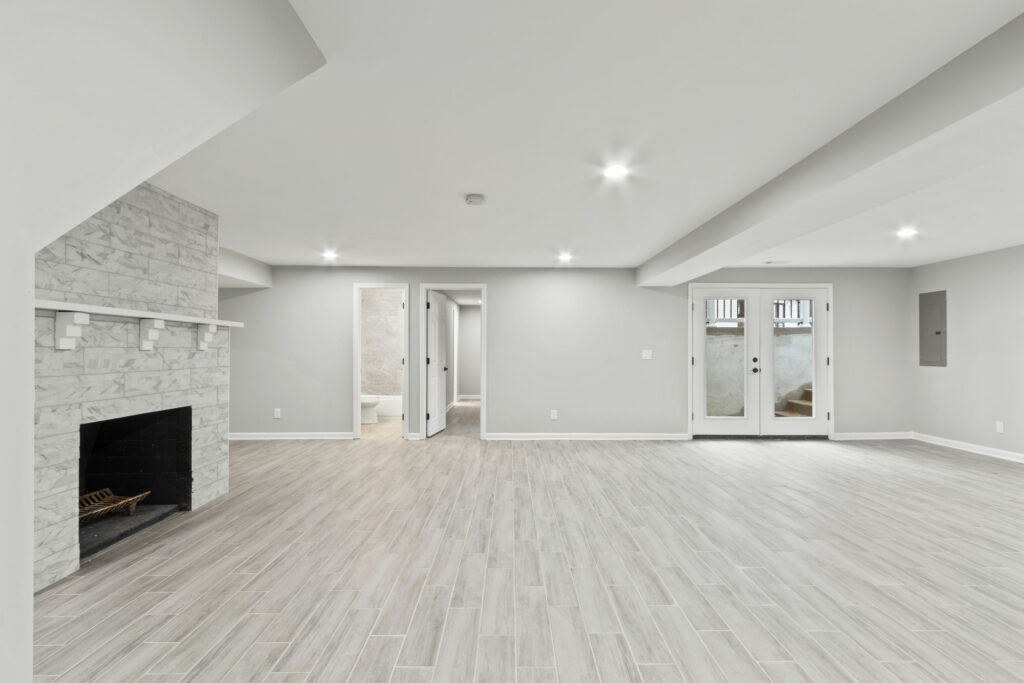 Open concept basement, with light plank floors, grey walls, pot lights, a fireplace, and modern feel